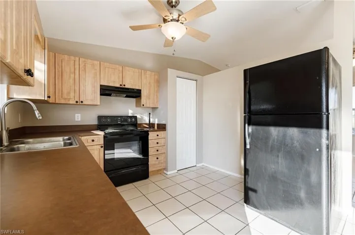Kitchen with lofted ceiling, light brown cabinets, black appliances, sink, and light tile patterned floors
