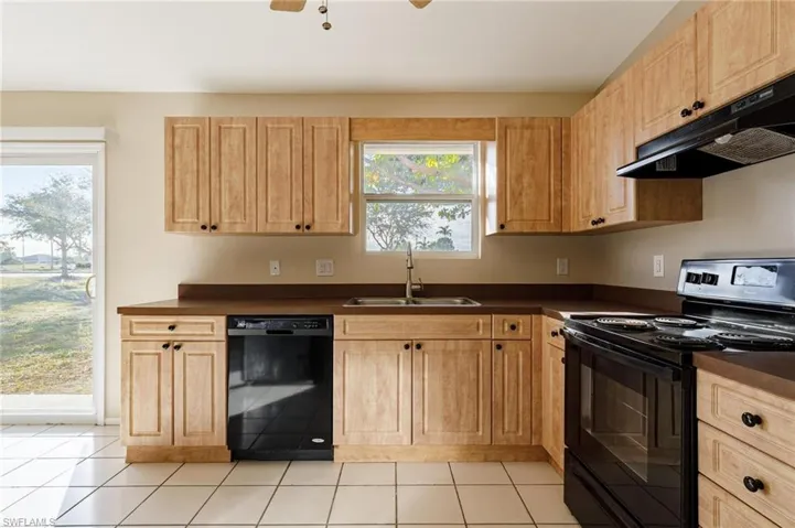 Kitchen featuring light tile patterned floors, black appliances, sink, and a wealth of natural light