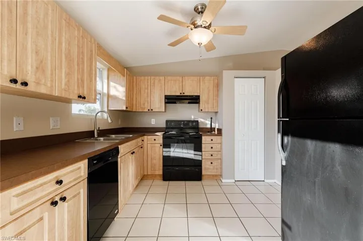 Kitchen featuring light tile patterned flooring, black appliances, sink, and vaulted ceiling