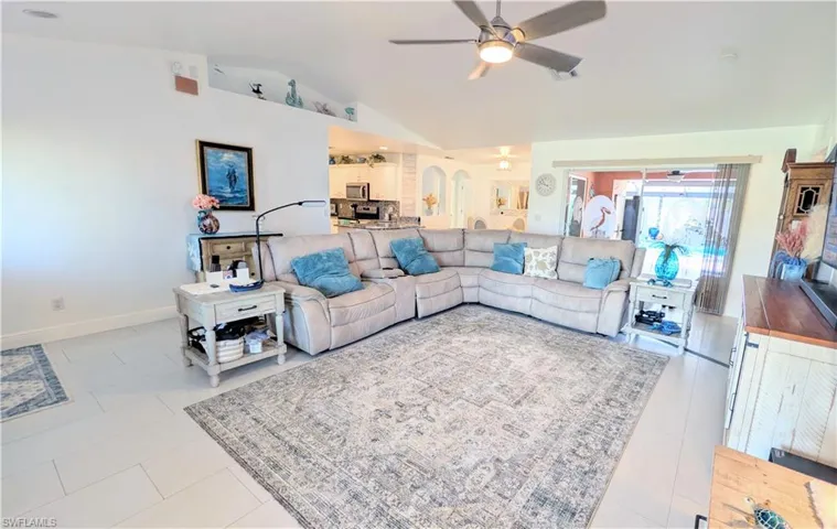 Spacious living area featuring light-toned tile flooring, vaulted ceilings, and a ceiling fan with integrated lighting