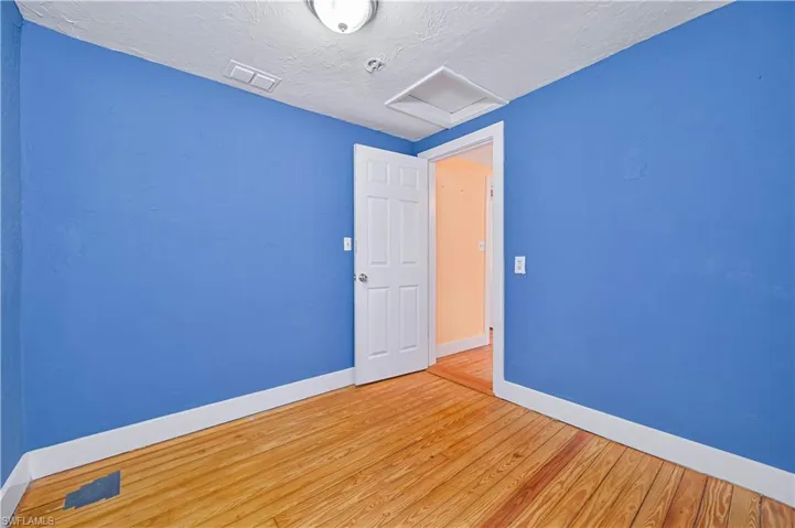 Spare room with baseboards, a textured ceiling, attic access, visible vents, and wood finished floors