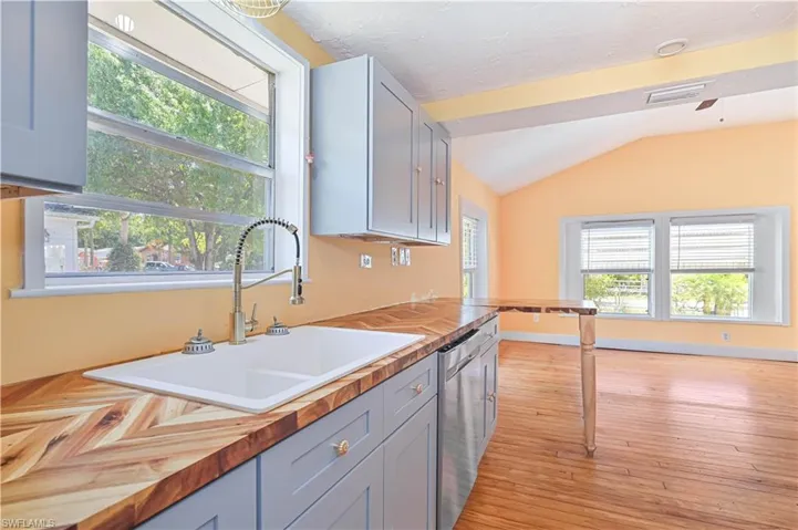 Kitchen with vaulted ceiling, visible vents, dishwasher, a sink, and wooden counters