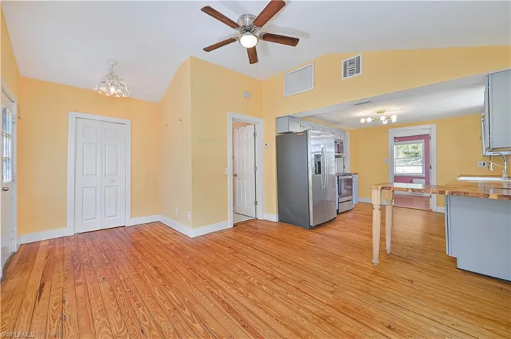 Unfurnished living room featuring light wood-type flooring, visible vents, lofted ceiling, ceiling fan with notable chandelier, and a sink