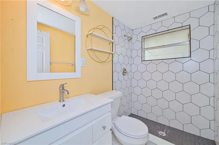 Full bathroom featuring a tile shower, vanity, visible vents, and toilet