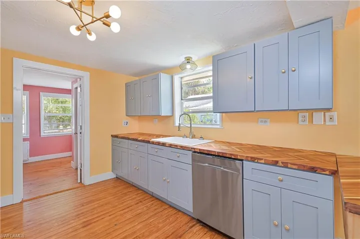 Kitchen with baseboards, a sink, wooden counters, light wood finished floors, and stainless steel dishwasher