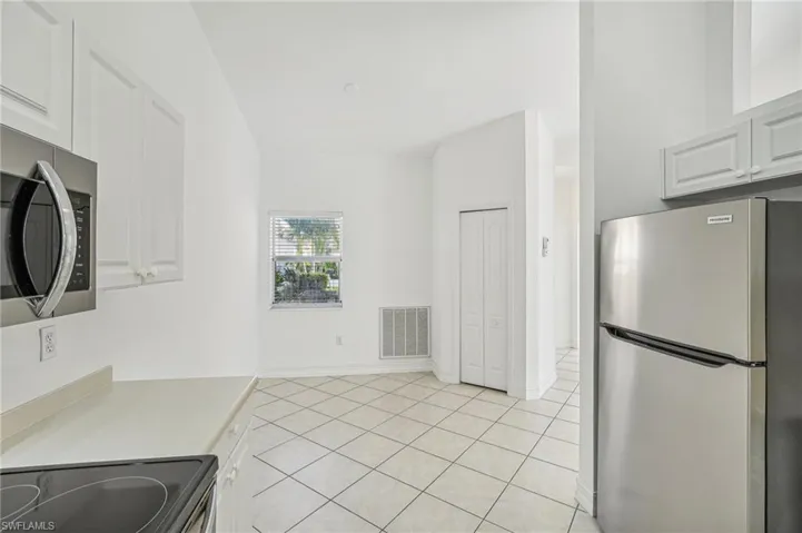 Kitchen featuring appliances with stainless steel finishes, white cabinetry, light countertops, light tile patterned floors, and baseboards