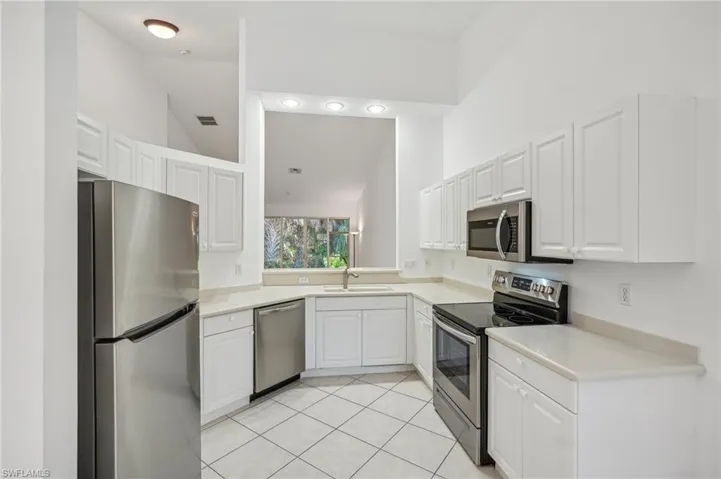 Kitchen featuring stainless steel appliances, a sink, lofted ceiling, white cabinets, and light countertops