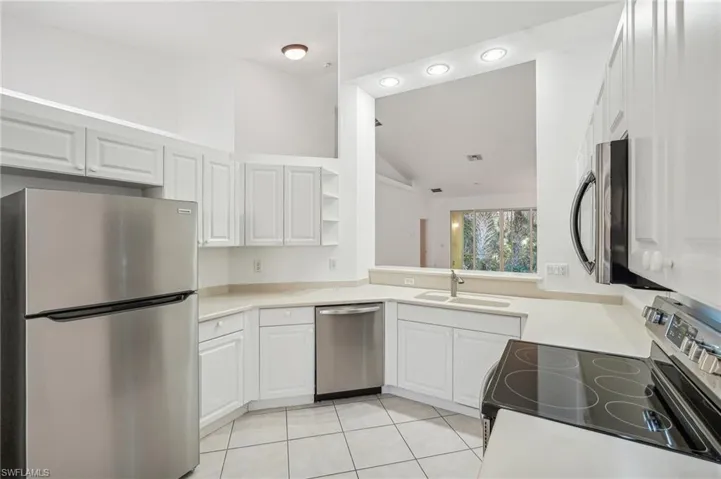 Kitchen featuring stainless steel appliances, a sink, light tile patterned flooring, vaulted ceiling, and open shelves