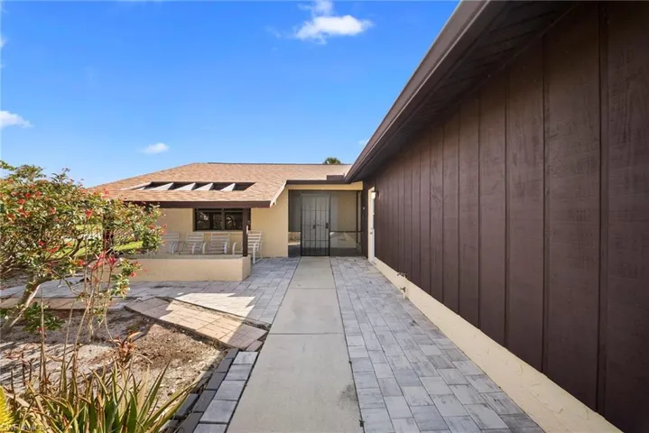 View of exterior entry featuring roof with shingles and a patio