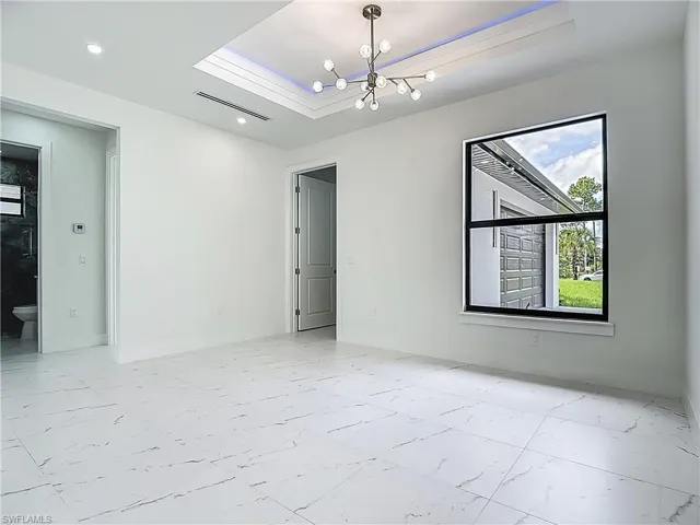 Spare room with light marble finish flooring, a raised ceiling, a chandelier, and recessed lighting