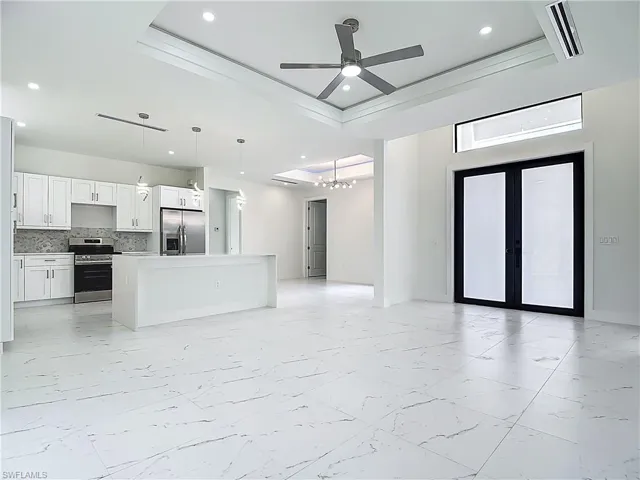 Unfurnished living room with light marble finish flooring, a tray ceiling, a chandelier, recessed lighting, and ceiling fan