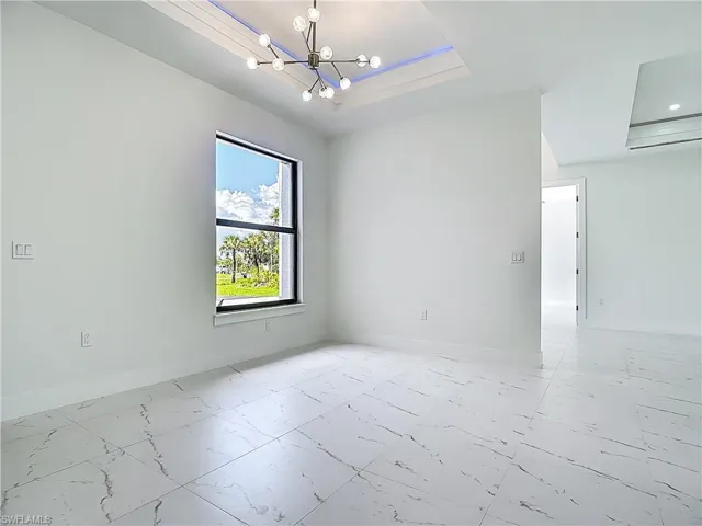 Unfurnished room with light marble finish flooring, a raised ceiling, and a chandelier
