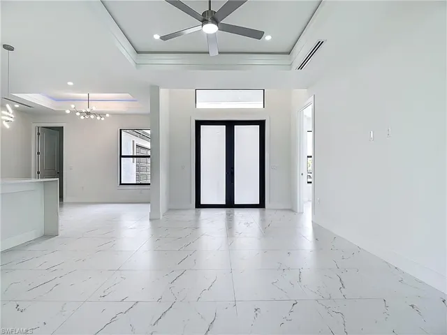 Foyer entrance featuring a tray ceiling, plenty of natural light, a chandelier, light marble finish flooring, and ornamental molding