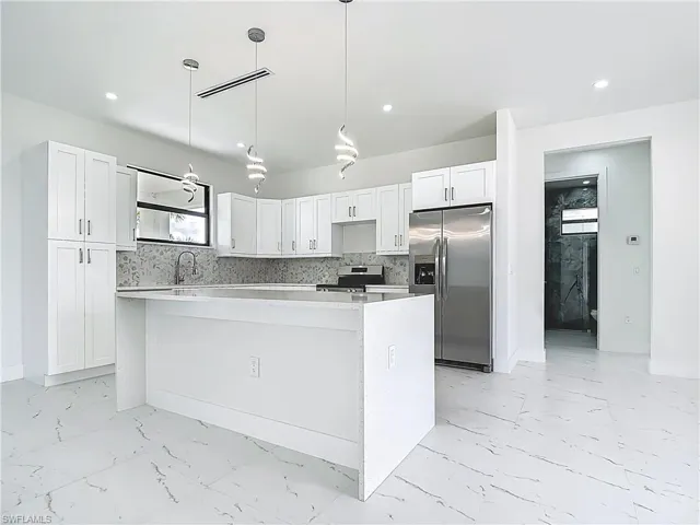 Kitchen with appliances with stainless steel finishes, light marble finish floors, a center island, white cabinets, and recessed lighting