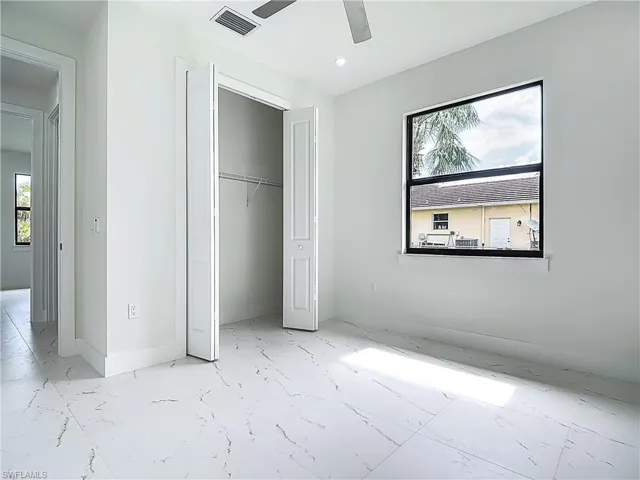 Unfurnished bedroom with multiple windows, marble finish floors, a closet, and ceiling fan