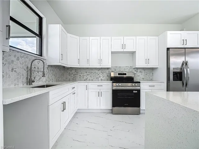 Kitchen featuring stainless steel appliances, light marble finish flooring, and white cabinets