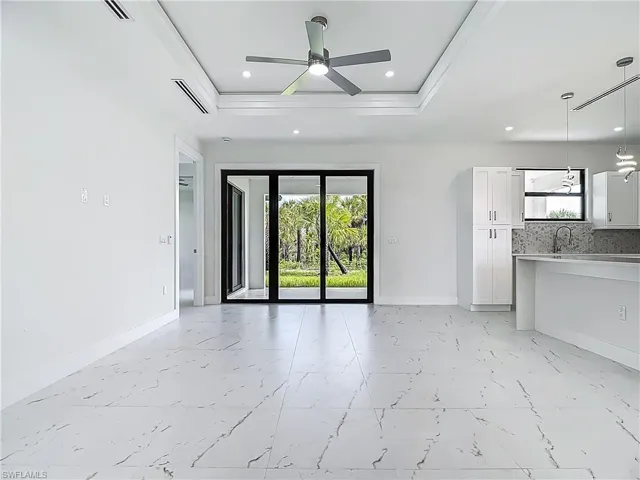Unfurnished living room with a raised ceiling, a ceiling fan, light marble finish flooring, recessed lighting, and ornamental molding