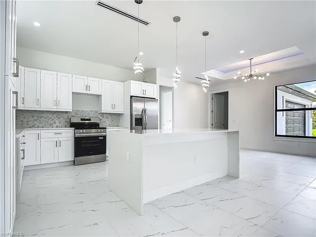 Kitchen featuring light marble finish flooring, stainless steel appliances, white cabinetry, a center island, and decorative light fixtures