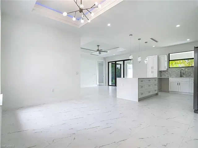 Unfurnished living room featuring a raised ceiling, plenty of natural light, recessed lighting, and a chandelier