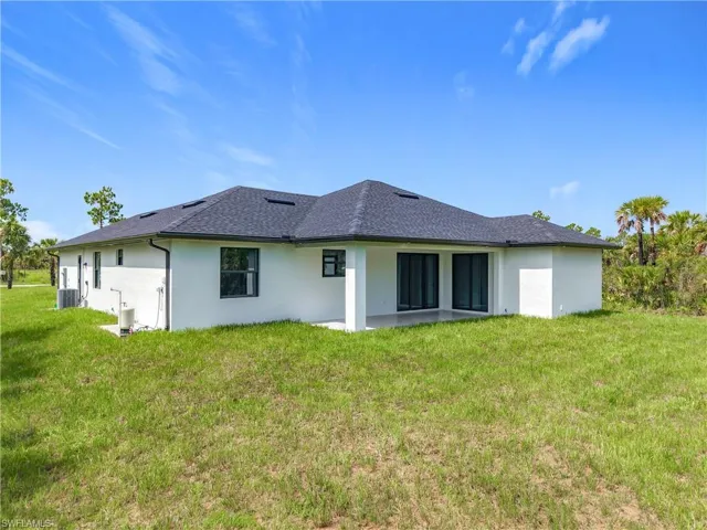 Rear view of property featuring stucco siding, a lawn, and roof with shingles