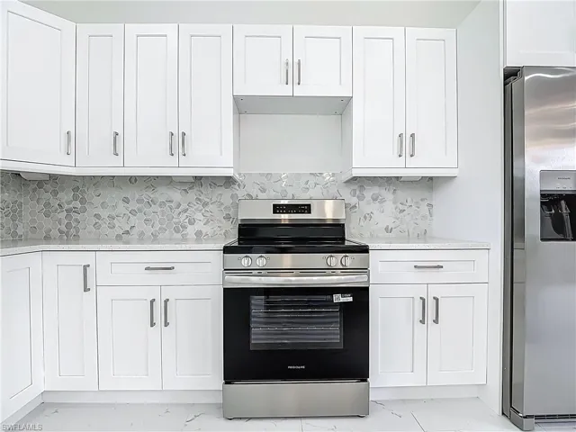 Kitchen with light marble finish flooring, appliances with stainless steel finishes, white cabinets, and decorative backsplash