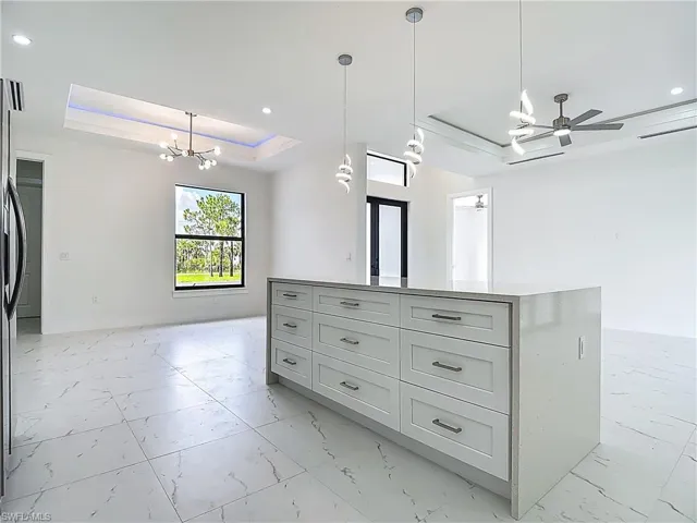 Kitchen with a raised ceiling, light marble finish flooring, a chandelier, open floor plan, and a center island
