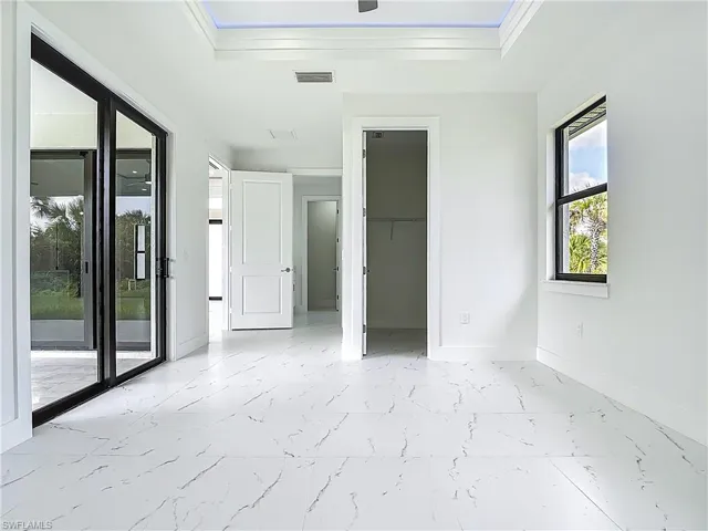 Unfurnished bedroom with light marble finish floors, access to outside, a tray ceiling, crown molding, and a closet