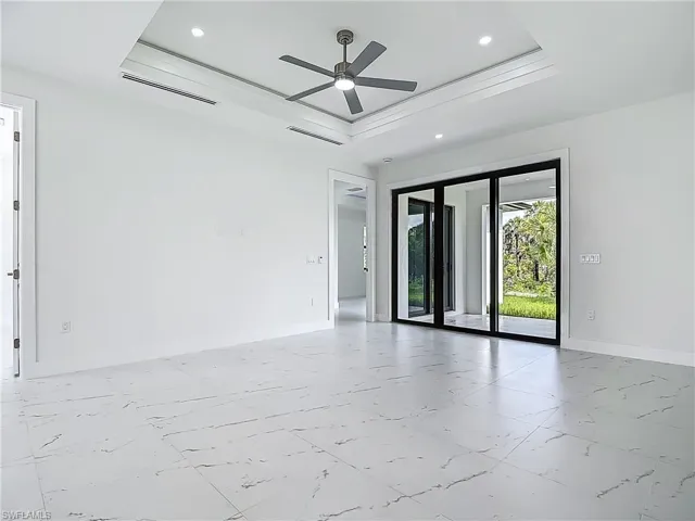 Empty room featuring a raised ceiling, marble look tile flooring, ceiling fan, and recessed lighting