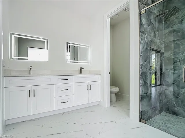 Full bath with marble finish flooring, a marble finish shower, and double vanity