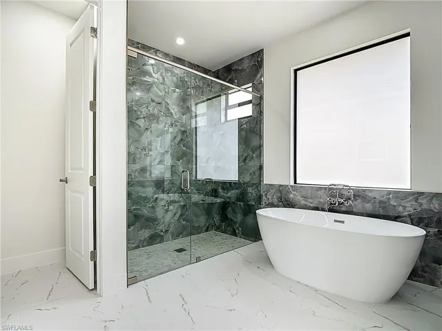 Bathroom with marble finish flooring, a freestanding bath, a marble finish shower, and recessed lighting