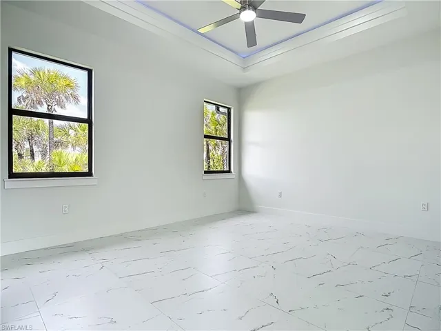 Empty room with marble finish flooring, ceiling fan, and a tray ceiling