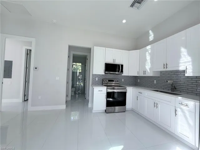 Kitchen with stainless steel appliances, white cabinetry, decorative backsplash, light tile patterned floors, and recessed lighting