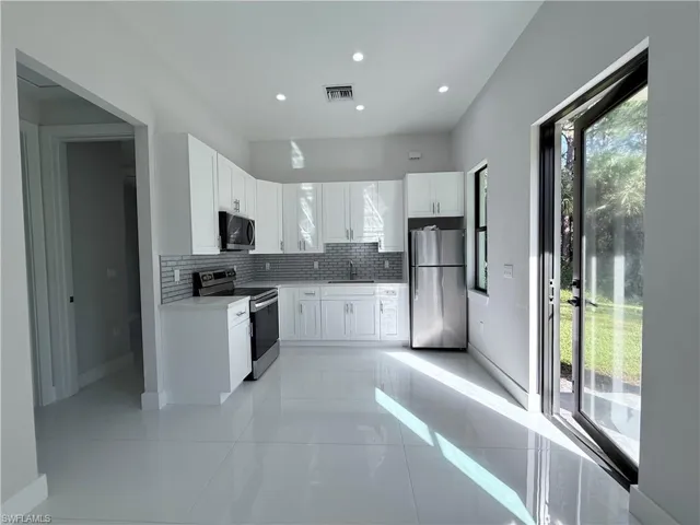 Kitchen with white cabinetry, backsplash, appliances with stainless steel finishes, recessed lighting, and light tile patterned flooring