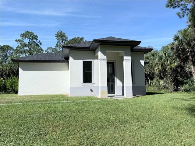 Back of house with a lawn, stucco siding, and roof with shingles