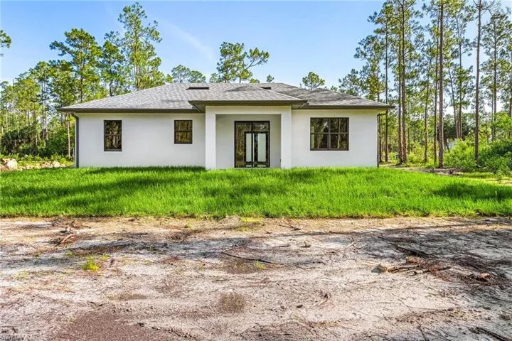 Back of property featuring stucco siding, a shingled roof, and a lawn