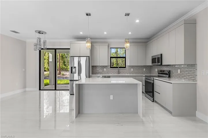 Kitchen featuring modern cabinets, a kitchen island, stainless steel appliances, light stone counters, and crown molding