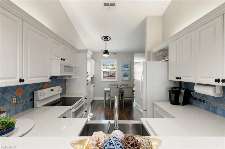 Kitchen featuring decorative backsplash, white cabinets, white appliances, and lofted ceiling