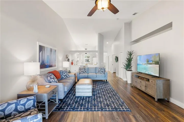 Living room with a ceiling fan, dark wood-style floors, and vaulted ceiling