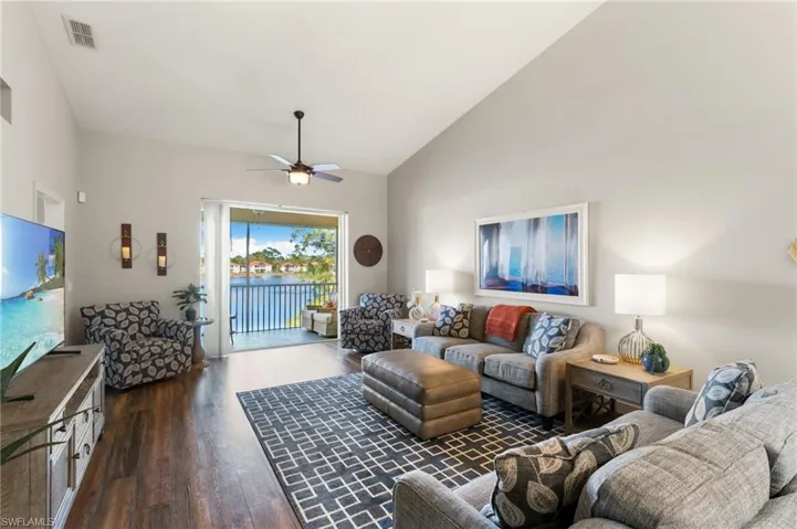 Living room featuring lofted ceiling, dark wood-style flooring, ceiling fan, and a water view