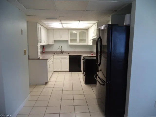 Kitchen with black appliances, a paneled ceiling, white cabinets, glass insert cabinets, and light tile patterned floors