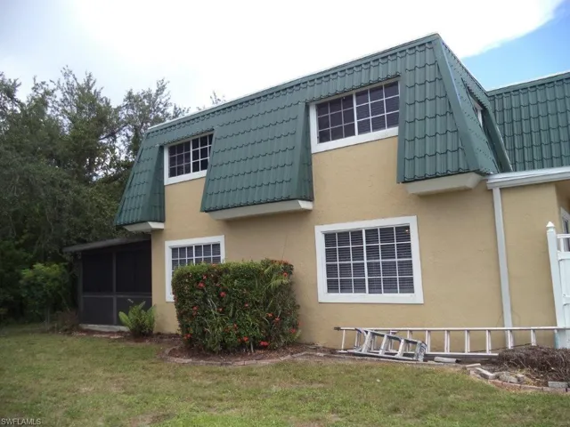 Rear view of house with stucco siding, a lawn, a tile roof, a sunroom, and mansard roof