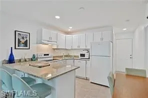 Kitchen featuring white appliances, a peninsula, under cabinet range hood, a breakfast bar, and white cabinets
