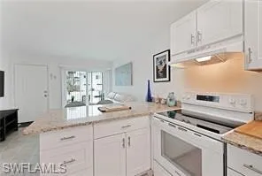 Kitchen with electric range, a peninsula, white cabinetry, under cabinet range hood, and open floor plan