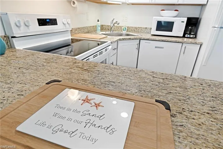 Kitchen with white appliances, white cabinetry, and light granite countertops