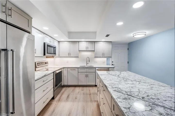 Kitchen featuring  lots of cabinets and drawer!  a dream kitchen with appliances with stainless steel finishes, recessed lighting, light stone countertops, light wood finished floors, and gray cabinetry
