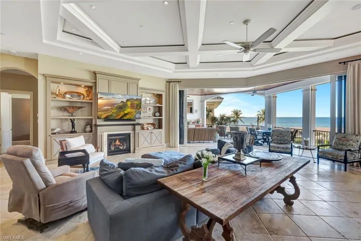 Living room with a glass covered fireplace, arched walkways, coffered ceiling, ceiling fan, and light tile patterned flooring