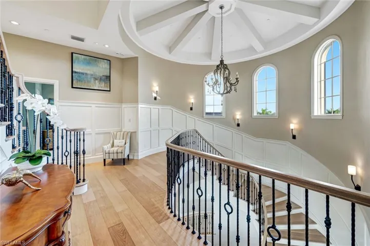 Hall with a decorative wall, a wainscoted wall, wood-type flooring, beamed ceiling, and a chandelier