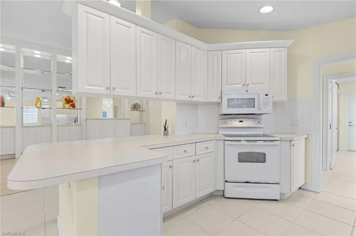 Kitchen with kitchen peninsula, white appliances, and white cabinets
