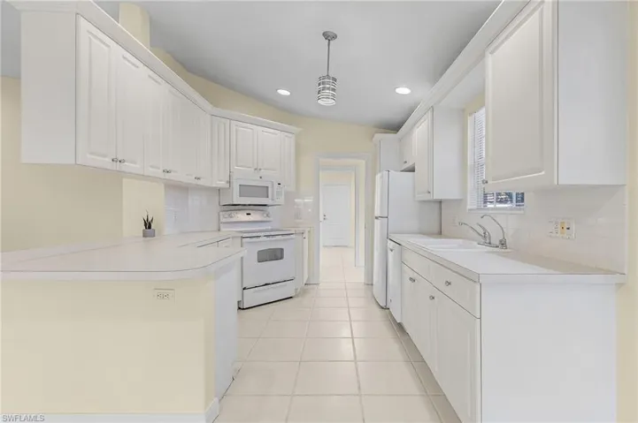 Kitchen featuring white cabinets, decorative light fixtures, white appliances, and sink