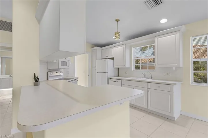 Kitchen with kitchen peninsula, white cabinets, pendant lighting, and white appliances
